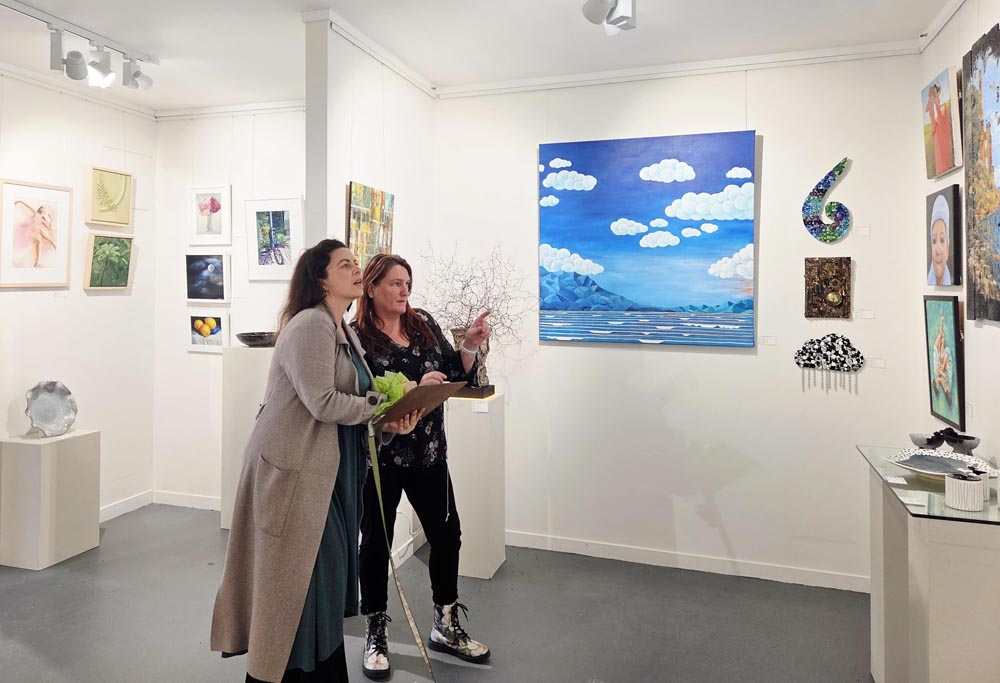 Jazz Lolesio and Kim Boyd, Managing Director of Estuary Arts, standing in a gallery and discussing the entries