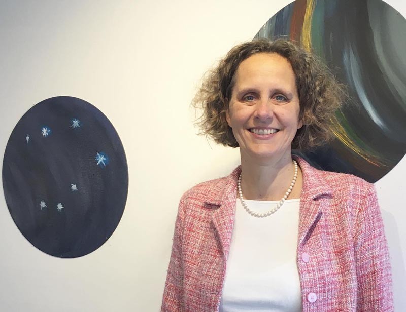Susanne Ritzenhoff standing in front of a white wall with two oval paintings hanging on it